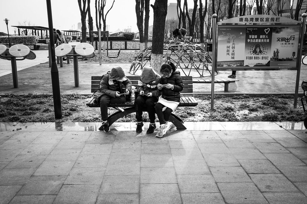 Des enfants chinois sont assis sur un banc dans la rue et jouent sur leur téléphone.